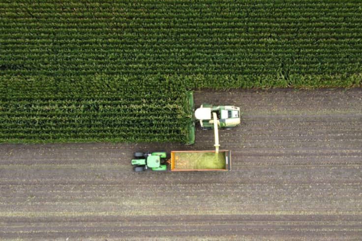 一架联合收割机在玉米地里装载拖拉机货物的鸟瞰图