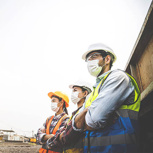 三名成年员工穿着个人防护装备(PPE)站在外面观察建筑工程. 