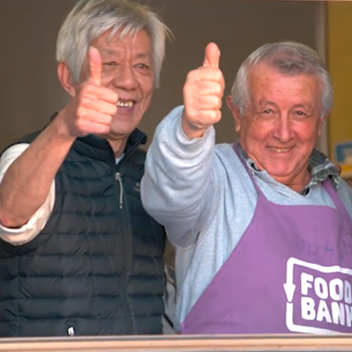 两名成年志愿者在社区早餐活动上竖起大拇指的照片.