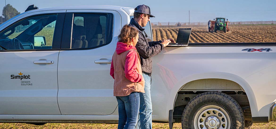 Image of Simplot Grower Solutions Crop Advisors standing with white pickup truck using laptop computer.