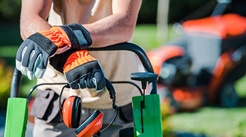 Landscaper wearing gloves, leaning on a push mower