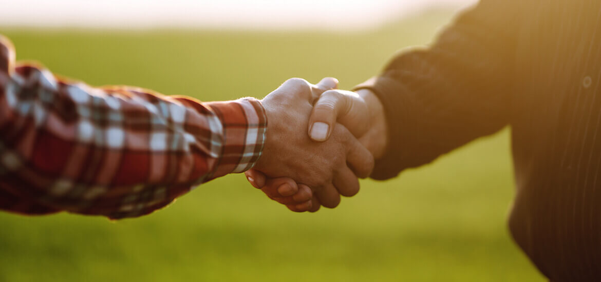 Image of two farmers shaking hands in the warm sunlight of sunrise.