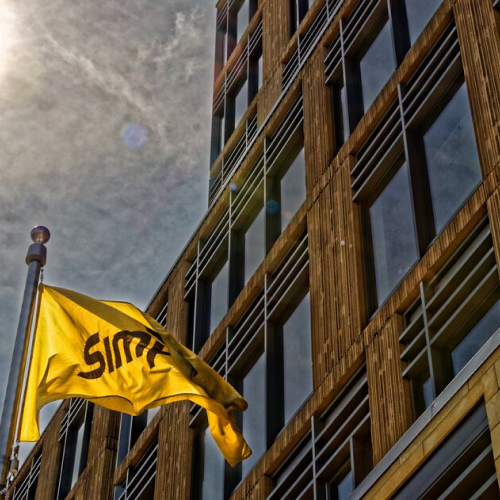 Photograph of J.R. Simplot Company World Headquarters building in Boise, Idaho with golden yellow Simplot flag flowing under partly cloudy sky.